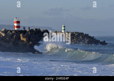 Fischer auf Steinpier mit Leuchttürmen, große Wellen krachen an der Küste von Nazare Portugal. Stockfoto