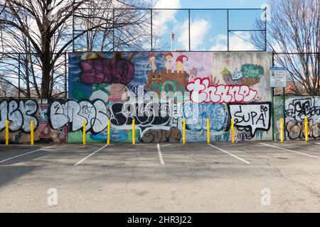 STADTLANDSCHAFT. Ein leerer Parkplatz in der Steinway Street mit einer bemalten Mauer, einem Zaun und einem blauen Himmel. In Astoria, Queens, New York City. Stockfoto