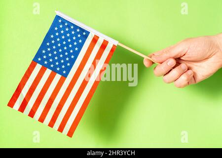 Hand mit kleiner amerikanischer Flagge auf grünem Hintergrund Stockfoto