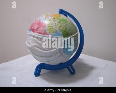 Die Welt mit einer Maske, um den Coronavirus nicht zu infizieren. Plastikspielzeug Globus mit Länderkarten Stockfoto