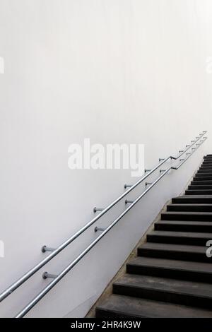 Leere Treppe, die mit einer Handschiene zwischen modernen Bürogebäuden hinauf führt. Stockfoto