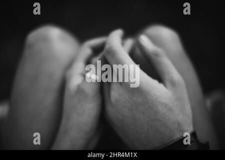 Liebe an dunklen Orten finden. Draufsicht Schwarz-Weiß-Bild von zwei Liebhabern, die die Hände halten. Stockfoto