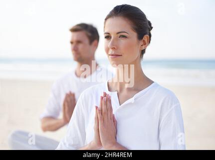Yoga am Meer. Ein junges Paar, das am Strand Yoga praktiziert. Stockfoto
