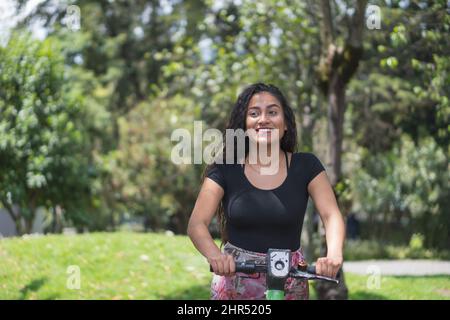 Junge hispanische Frau auf einem Roller in einem Park Stockfoto