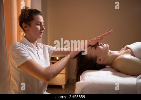 Weibliche Therapeutin massiert die Stirn eines entspannten Klienten an eine junge Frau. Entspannende Massage. Massotherapie. Alternative Medizin. Wellnessbehandlungen. Stockfoto