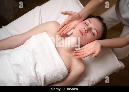 Gesichtsmassage für Frauen im Spa-Salon, Draufsicht, Hände des Massagetherapeuten auf dem Gesicht des Mädchens, Hautverjüngungsmassage, Gesundheits- und Jugendkonzept Stockfoto