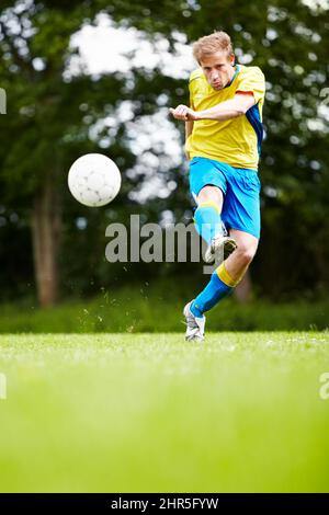 Biegen Sie den Ball in Richtung eines Tores. Aufnahme eines Fußballspielers, der den Ball mit Gusto tritt. Stockfoto