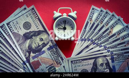 Draufsicht auf weißen Wecker und Banknoten auf rotem Hintergrund. Konzept für den Kopierraum Stockfoto