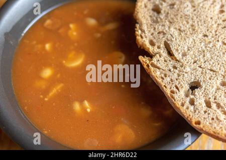 Gulaschsuppe in einer schwarzen Schüssel mit einer Scheibe grauem Brot auf einem Holztisch Stockfoto