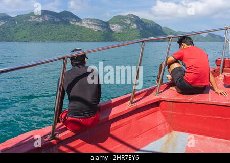 Rückansicht des asiatischen Mannes im schwarzen Hemd, der sich auf dem Balkon entspannt und den Blick vom Boot auf die Insel Samui im Meer genießt. Fröhliche, zwanglose männliche Touristen draußen auf tr Stockfoto