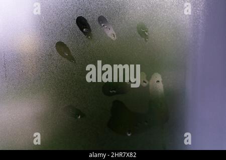 Kleiner Kinderhanddruck auf einem nebligen regnerischen Glas. Stockfoto