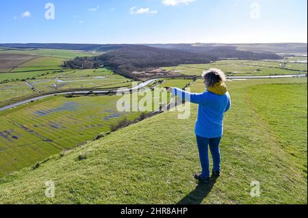 Brighton UK 25. February 2022 - Ein Spaziergänger genießt die Aussicht über den Fluss Cuckmere und das Tal unterhalb von Alfriston , Sussex an einem schönen sonnigen Tag : Credit Simon Dack / Alamy Live News Stockfoto