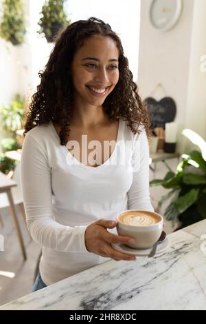 Lächelnd schöne junge afroamerikanische Frau hält Kaffeebecher, während sie im Café steht Stockfoto