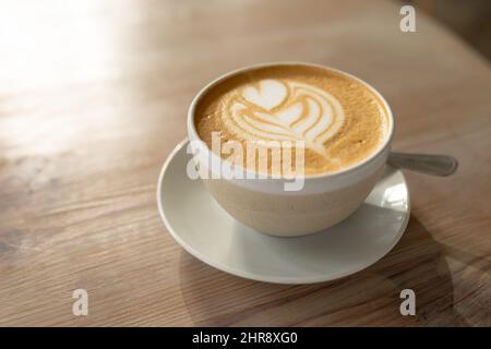 Nahaufnahme von frischem Cappuccino aus großer Perspektive mit Schaumkunst, serviert in einem Becher auf dem Tisch im Café Stockfoto