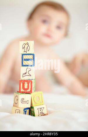 Bauen Sie heute auf die Zukunft Ihrer Kinder auf. Ein Turm aus Bausteinen im Vordergrund mit einem niedlichen Baby im Hintergrund. Stockfoto