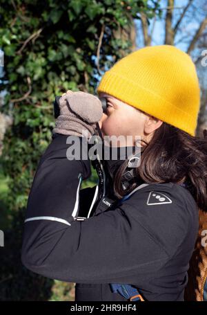 Person mit Hut und Handschuhen Vogelbeobachtung an einem sonnigen Wintertag in der Natur Stockfoto