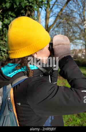 Person mit Hut und Handschuhen Vogelbeobachtung an einem sonnigen Wintertag in der Natur Stockfoto