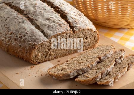 Laib Pavé-Brot, Mehrkornbrot und Scheiben aus nächster Nähe auf einem hölzernen Schneidebrett Stockfoto