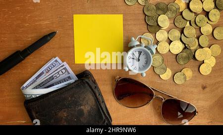 Blick von oben auf Brieftasche, Banknoten, Münzen, Wecker, Gläser und Stift auf Holzschreibtisch. Konzept für den Kopierraum Stockfoto