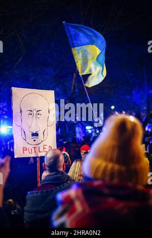 Ukrainische Flagge und ein Plakat mit einer Karikatur von Wladimir Putin, das als Adolf Hitler dargestellt und während der Demonstration mit der Beschriftung „Putler“ versehen wurde. Nach dem Beginn der russischen Invasion in der Ukraine protestierten Mitglieder der ukrainischen Gemeinschaft sowie unterstützende Polen und Belarussen in der Nähe der diplomatischen Vertretungen der Russischen Föderation, um ihre Opposition gegen die russische militärische Aggression zum Ausdruck zu bringen. In Krakau, wo die ukrainische Einwanderung besonders zahlreich ist, versammelten sich mehrere tausend Menschen vor dem russischen Konsulat. Stockfoto