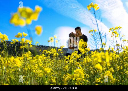 Ein Blick auf ein junges, spanisch engagiertes Paar, das sich in einem Blumenfeld amüstet Stockfoto