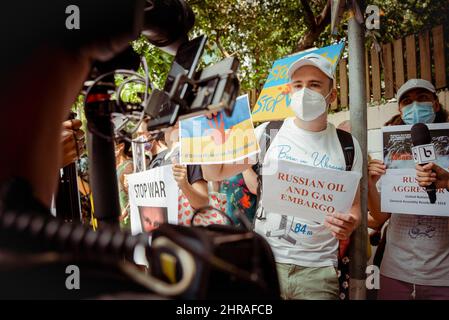 Bangkok, Thailand. 25.. Februar 2022. Ein Mann mit weißer Baseballmütze und Maske hält Plakate für Reporter, die während der Demonstration 'russisches Öl- und Gasembargo' und '#StopRussianAggression' lesen. Demonstranten versammelten sich vor der russischen Botschaft in Bangkok, um die russische Invasion in die Ukraine zu verurteilen. Über fünfzig standen vor den Toren der Botschaft, sangen die ukrainische Nationalhymne und hielten Zeichen, die Sanktionen und Öl- und Gasembargos forderten. Kredit: SOPA Images Limited/Alamy Live Nachrichten Stockfoto