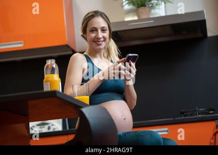 Schwanger blonde Frau trinken einen Orangensaft in der Küche und telefonieren Stockfoto