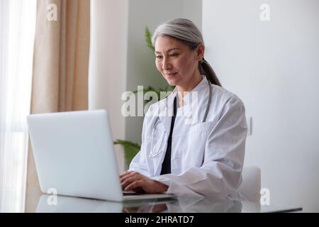Fokussierte medizinische Fachärztin, die im Büro auf einem Laptop tippt Stockfoto
