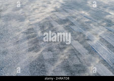 Wind über die schneebedeckte Straße mit Radmarkierungen Stockfoto