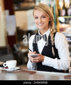 Service mit einem Lächeln. Porträt einer attraktiven Kellnerin, die Kaffeesorders für den Morgen entgegennimmt. Stockfoto