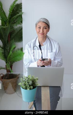 Lächelnder Arzt im Büro mit Laptop auf dem Schreibtisch Stockfoto
