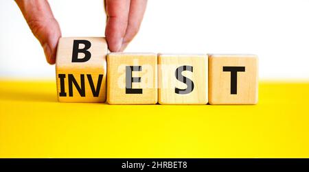 Symbol für beste Investition. Geschäftsmann dreht einen Holzwürfel und ändert das Wort Invest in Best. Schöner gelber Tisch, weißer Hintergrund. Business und das beste i Stockfoto