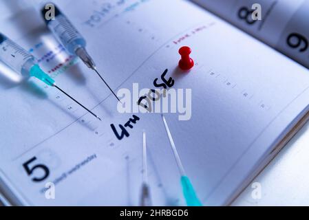 Covid-Impfkampagne „4th Dosis“ und Jab-Konzept auf der Tagesordnung. Spritze auf Kalender mit als Konzept für die vierte Covid-19-Impfstoffdosis zur Bekämpfung der Stockfoto