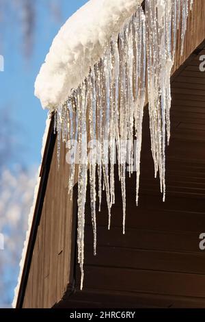 Eiszapfen hängen vom Dach auf dem blauen Himmel Hintergrund Stockfoto