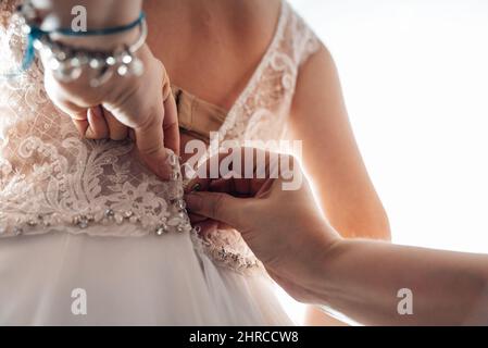 Nahaufnahme der weiblichen Hände, die das Hochzeitskleid auf einer Braut aufziehen Stockfoto