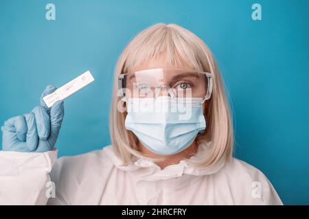 Arzt in medizinischem PSA-Anzug, blaue Handschuhe mit Schnellantigen-Testkit mit negativem Ergebnis während des Abstrichs COVID-19-Tests. Stockfoto