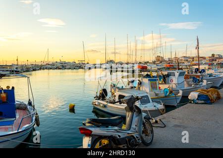 Farbenfrohe rote, weiße und blaue Fischerboote säumen bei Sonnenuntergang den Hafen der griechischen Insel Aegina, Griechenland. Stockfoto