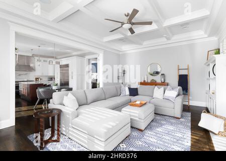 Ein wunderschönes Wohnzimmer mit gemütlichen Möbeln und einer Kassettendecke mit Blick auf ein luxuriöses Esszimmer und Küche. Stockfoto