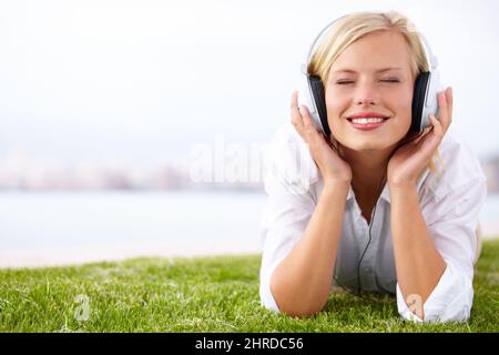 Ich liebe dieses Lied. Aufnahme einer Frau, die mit geschlossenen Augen auf einem Wiese liegt und Musik hört. Stockfoto