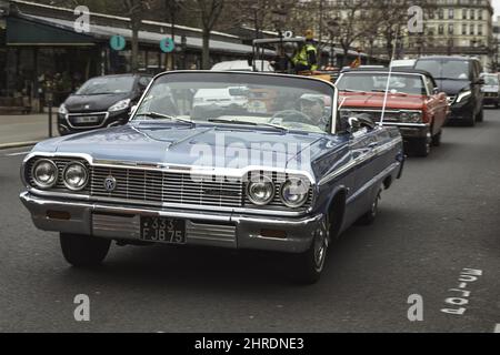 Mann, der das klassische blaue Chevrolet Impala Cabriolet aus dem Jahr 1964 auf der Straße fährt Stockfoto