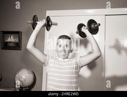 1950S JUNGE MIT CREWCUT FRISUR TRAINING HEBEN PAAR HANTELN FREI GEWICHTE IN JEDER HAND BLICK AUF DIE KAMERA - J1121 DEB001 HARS GESUNDER BALANCE LIFESTYLE ZUFRIEDENHEIT GESUNDHEIT HEIM LEBEN KOPIEREN RAUM HALBE LÄNGE KÖRPERLICHE FITNESS PERSONEN INSPIRATION GEWICHTE MÄNNER VERTRAUEN AUSDRÜCKE B&W AUGENKONTAKT ZIELE AKTIVITÄT KÖRPERLICHE WELLNESS ABENTEUER STÄRKE FRISUR ERHOLUNG STOLZ FREIE HANTEL FLEXIBILITÄT MUSKELN STILVOLL TEENAGED DEB001 CREWCUT FOKUSSIERTEN WACHSTUM JUGENDLICHE PRE-TEEN PRE-TEEN JUNGEN STAMM SCHWARZ UND WEISS KAUKASISCHEN ETHNIE KONZENTRIERT ALTMODISCH Stockfoto