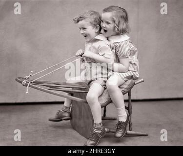 1930S LACHEND LÄCHELNDER JUNGE UND MÄDCHEN SITZEN AUF DER RÜCKSEITE DES WINDSOR STUHLS UND GEBEN VOR, ES SEI EIN PFERD ODER EINE KUTSCHE ODER SOGAR EIN WINTERSCHLITTEN - J3228 HAR001 HARS FEMALS BROTHERS STUDIO SHOT SCHLITTEN GESUNDHEIT HEIM LEBEN KOPIEREN RAUM FREUNDSCHAFT IN VOLLER LÄNGE PERSONEN MÄNNER GESCHWISTER SCHWESTERN B&W CARRIAGE ZÜGEL GLÜCK FRÖHLICH UND GESCHWISTER VORGEBLICH FREUNDLICH IMAGINÄRE PHANTASIE FRÖHLICH IMAGINED ODER WINDSOR KREATIVITÄT SCHWARZ-WEISSE KAUKASISCHE ETHNIE SOGAR HAR001 MACHEN GLAUBEN ALTMODISCH Stockfoto