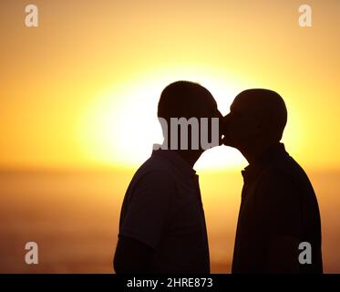 Glückselige Sonnenuntergang Kuss - Homosexuell paar. Sihlouette Porträt eines homosexuellen Paares, das sich vor einem Sonnenuntergang küsst - Copyspace. Stockfoto