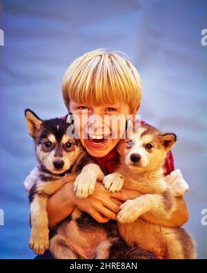 1950S 1960S LÄCHELNDER BLONDER JUNGE MIT ZWEI WELPEN ALASKAN MALAMUTEN BLICK IN DIE KAMERA - KD1225 DEB001 HARS AUGENKONTAKT TRÄUME GLÜCK SÄUGETIERE KOPF UND SCHULTERN FRÖHLICHES ABENTEUER HUNDE AUFREGUNG STOLZ LÄCHELT POOCH KONZEPTUELLE RASSE FRÖHLICHE RASSEN DEB001 HUNDE JUGENDLICHE SÄUGETIERE PRE-TEEN PRE-TEEN JUNGE PUP ALASKAN KAUKASISCHE ETHNIE ALTMODISCH Stockfoto