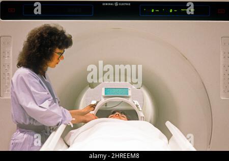 1980S MEDIZINTECHNIKER MIT PATIENT, DER EINEN KERNSPINTOMOGRAPHIE-MRT-SCANNER BETREIBT - KM7760 GER002 HARS HEALTHCARE BERUF, DER ARBEITET PRÄVENTION ANBIETER HIGH-ANGLE-ANBIETER ENTDECKUNG PRAKTIKER HEILUNG DIAGNOSE AUFREGUNG WISSEN LEISTUNGSSTARKE INNOVATION GESUNDHEIT BEEINTRÄCHTIGUNG BERUFE BEHANDLUNG HEILER KONZEPTIONELL PRAKTIKER RESONANZ-SCANNER MRI-BILDGEBUNG ZUSAMMENARBEIT MID-ADULT PROFIS KAUKASISCHE ETHNIZITÄT KRANKHEIT MAGNETISCH ALTMODISCH Stockfoto