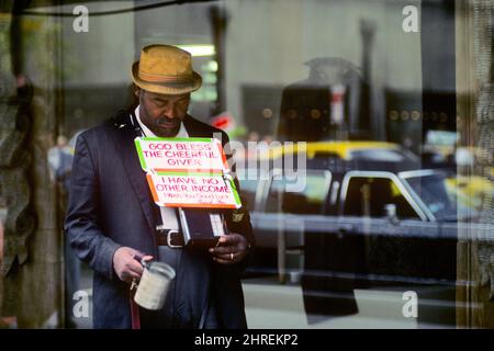 1980S BLINDER AFROAMERIKANISCHER BETTLER AUF DEM BÜRGERSTEIG VON NEW YORK CITY MIT EINER SCHWARZEN LIMOUSINE, DIE SICH IM FENSTER HINTER IHM WIDERSPIEGELT - KS18658 BLC001 HARS HIM VERARMTE, NACHDACHTE BETTLER ALTMODISCHER AFROAMERIKANISCHER AMERIKANER Stockfoto