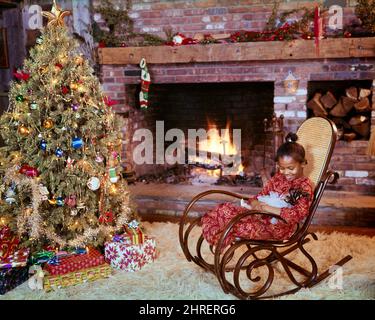 1970S AFRIKANISCH-AMERIKANISCHES MÄDCHEN MIT PUPPE, DIE IN GEBOGENEM HOLZSCHAUKELSTUHL AM KAMIN SITZT UND MIT WEIHNACHTSBAUM GESCHMÜCKT IST - KX7595 PHT001 HARS SKYLINE JUVENILE NIEDLICHE EVE SCHAUKEL DEKORATIONEN FREUDE LIFESTYLE FEIER FRAUEN ROCKER HEIM LEBEN KOPIEREN RAUM VOLLER LÄNGE GELASSENHEIT DEKORIERT MORGEN WEITWINKEL GLÜCK FRÖHLICH WOHNZIMMER AFROAMERIKANER FRÖHLICH AFROAMERIKANER UND FORTSCHRITT ERHOLUNG SCHWARZ ETHNIZITÄT STOLZ DURCH IN ERWARTUNG LÄCHELT DEZEMBER KONZEPTUELL DEZEMBER 25 BENT FREUDVOLLES WACHSTUM JUVENILE ALTMODISCHE AFROAMERIKANER Stockfoto