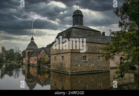 Wasserburg in dramatischem Himmel mit Blitz im Hintergrund. Schöne Reflexion im Wasser Stockfoto