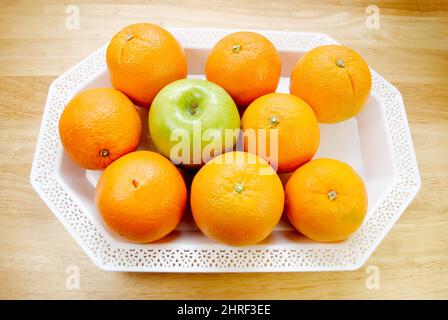 Mehrere Orangen auf einer weißen Platte mit einem grünen Apfel Stockfoto