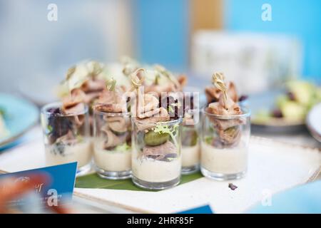 Köstliche Snacks mit Oliven und Fleisch in Glassbechern auf dem Banketttisch für ein Buffet. Delikatessen aus der Nähe, Vorspeise, Antipasti. Stockfoto